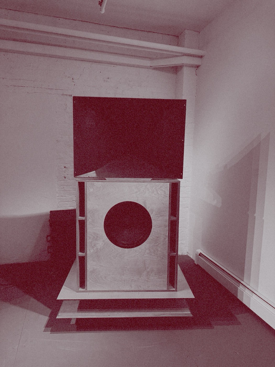 The Prima Stack from the front against a white brick wall: a horn on a plywood woofer cabinet on a stepped plinth, duotone pink on silver